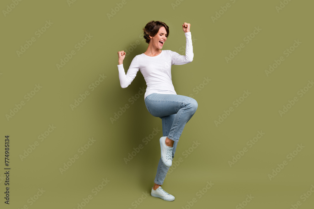 Full length photo of overjoyed young girl raise fists celebrating victory luck delight close eyes isolated khaki green color background Full length photo of overjoyed young girl raise fists celebrating victory luck delight close eyes isolated khaki green color background
