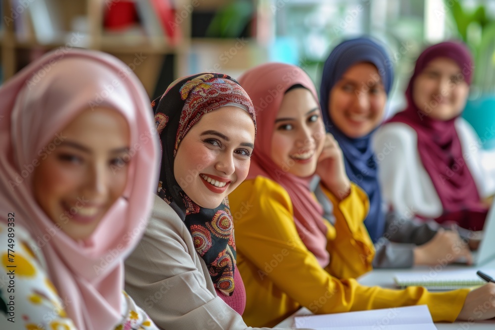 Empowered collaboration: Group of hijab-wearing women smile and work together at a table with laptops