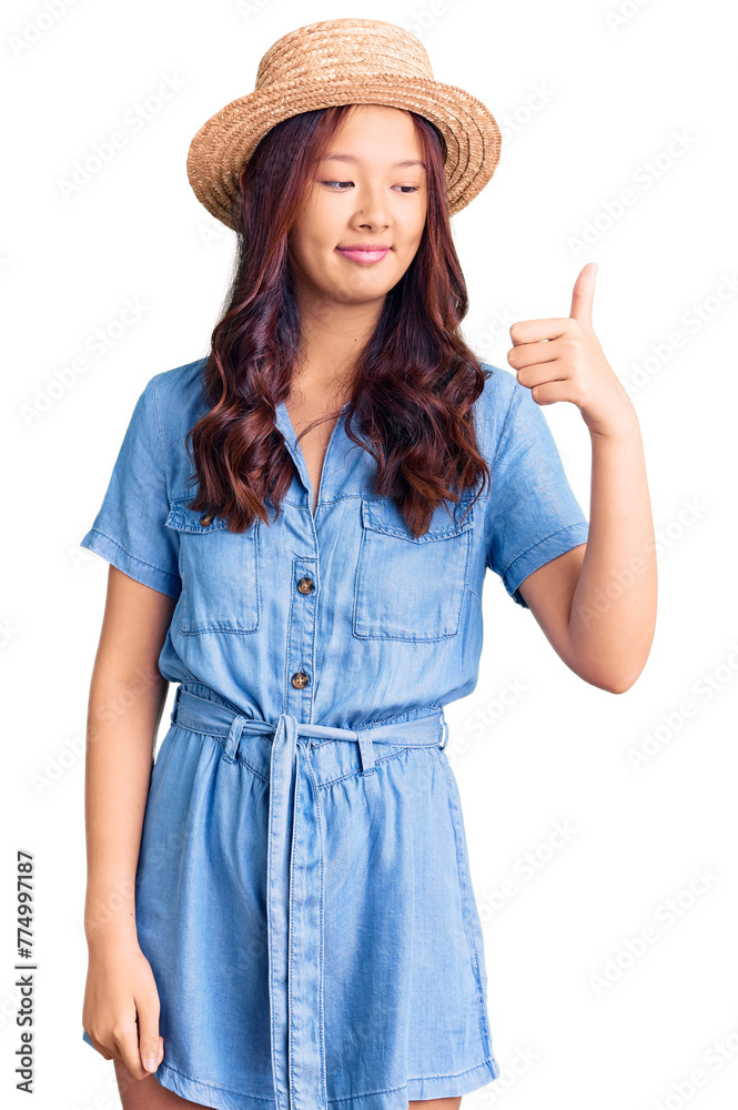 Young beautiful chinese girl wearing summer hat looking proud, smiling doing thumbs up gesture to the side Young beautiful chinese girl wearing summer hat looking proud, smiling doing thumbs up gesture to the side