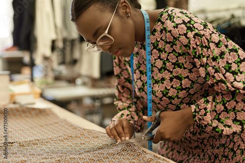 African female fashion designer cutting cloth at a studio workbench