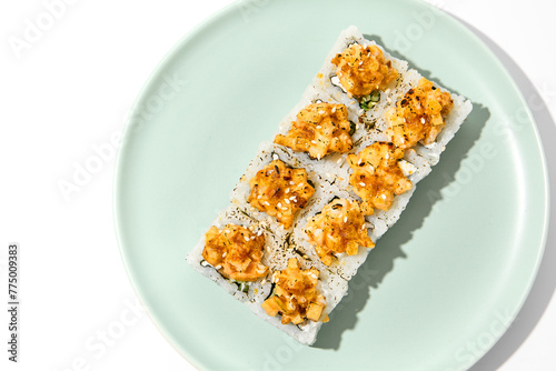 Sushi topped burnt shrimp tartare. Maki sushi with shrimp and spicy sauce on ceramic plate Baked maki roll topped shrimp tartare isolated on white background with hard shadow