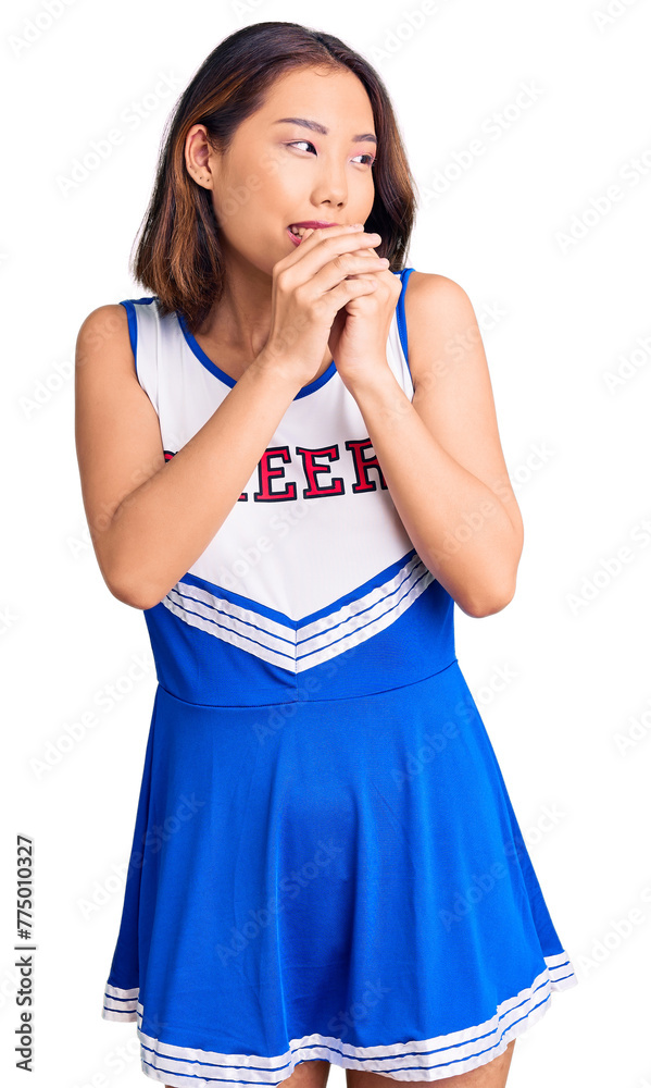 Young beautiful chinese girl wearing cheerleader uniform laughing nervous and excited with hands on chin looking to the side Young beautiful chinese girl wearing cheerleader uniform laughing nervous and excited with hands on chin looking to the side