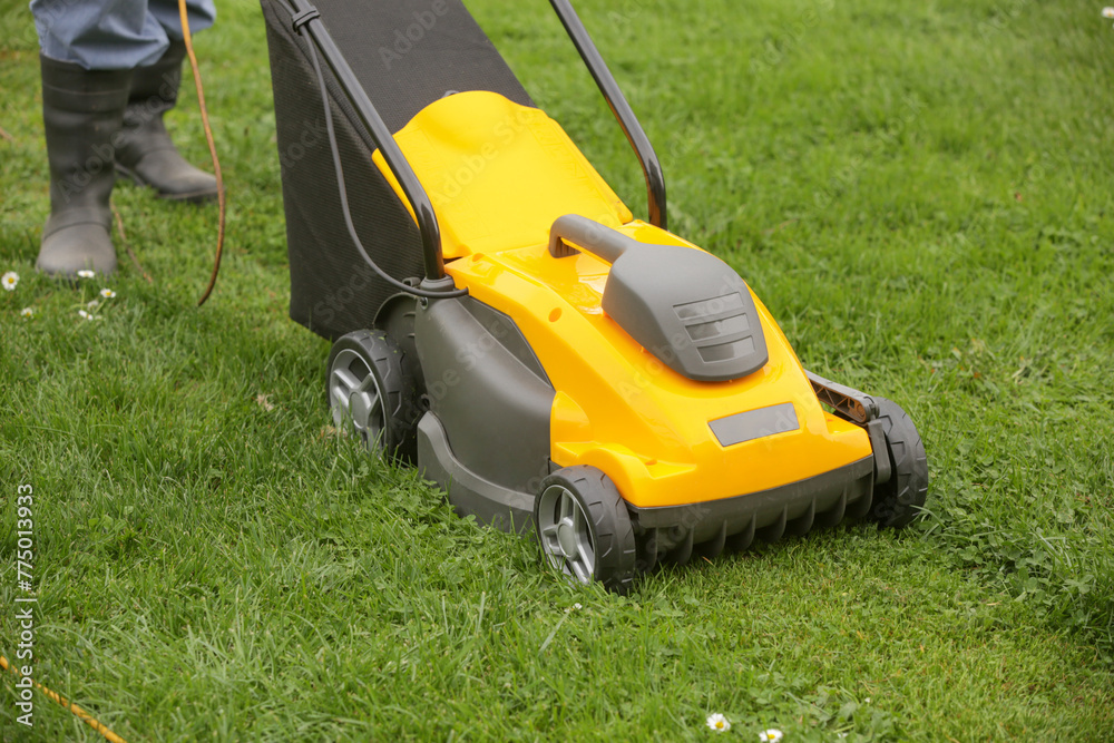 Gardener in black rubber boots trimming lawn with mower Gardener in black rubber boots trimming lawn with mower