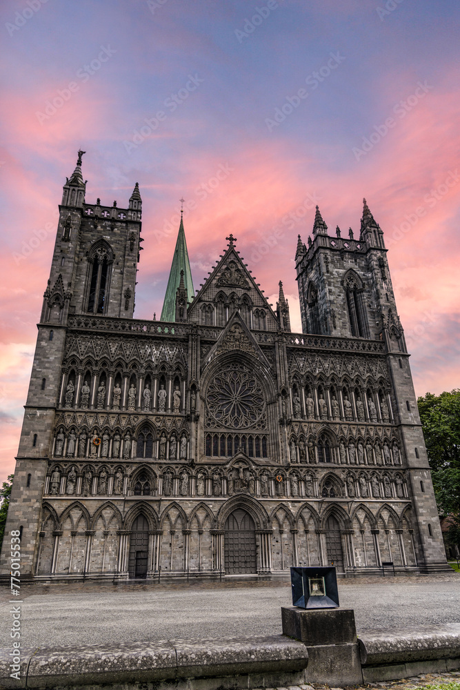 Sunset over the Nidaros Cathedral in Trondheim, Norway. The facade with statues and church spires stands against a vibrant evening sky