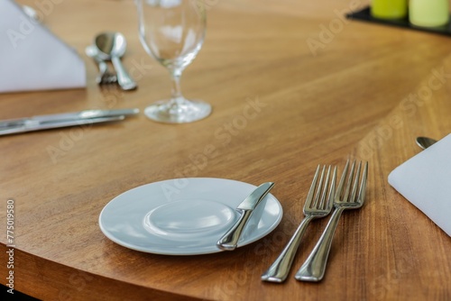 Plate, fork, spoon, cutlery, dining table on a wooden table in a restaurant, closeup shot