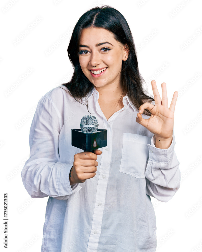 Beautiful hispanic woman holding reporter microphone doing ok sign with fingers, smiling friendly gesturing excellent symbol Beautiful hispanic woman holding reporter microphone doing ok sign with fingers, smiling friendly gesturing excellent symbol