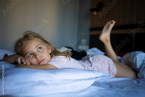 Cute blonde little girl in beautiful pajamas on a big and cozy bed after a night's sleep. A good mood is a charge of cheerfulness