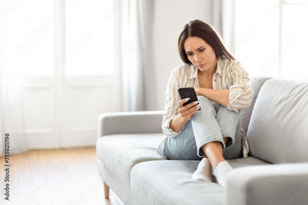 Pensive woman with smartphone on couch at home Pensive woman with smartphone on couch at home