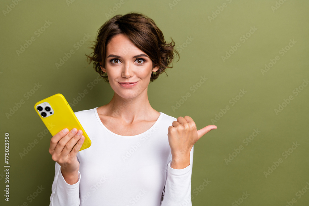 Photo portrait of lovely young lady hold telephone point empty space wear trendy white garment isolated on khaki color background Photo portrait of lovely young lady hold telephone point empty space wear trendy white garment isolated on khaki color background