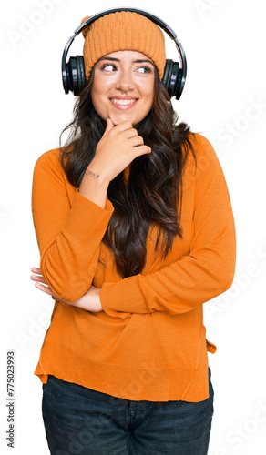 Beautiful brunette young woman listening to music using headphones with hand on chin thinking about question, pensive expression. smiling with thoughtful face. doubt concept. © Krakenimages.com