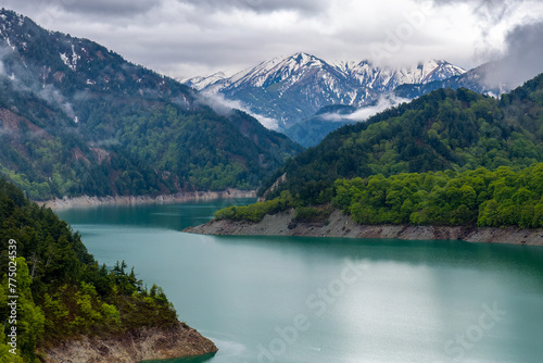 Snow covered mountain peaks and stormy skies over a forest and lake (Lake Kurobe, Japan)