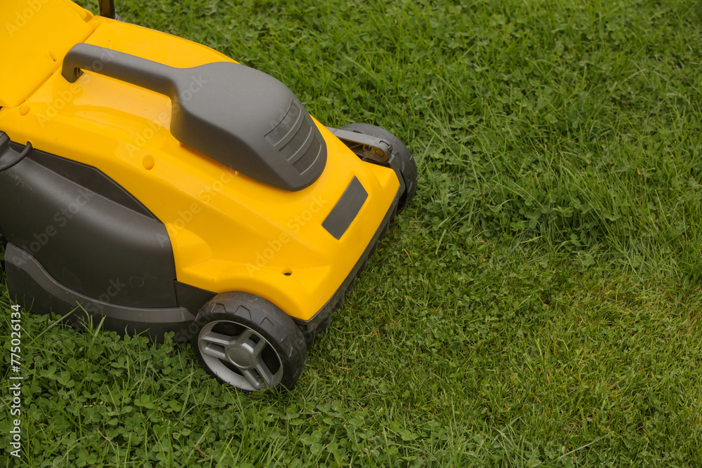 Yellow lawn mower on the spring green grass in the yard