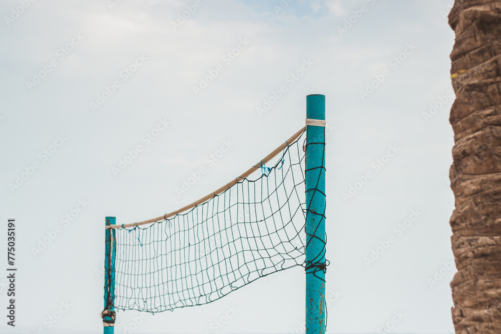 Volleyball net with blue poles next to brown palm ttree under light blue sky Volleyball net with blue poles next to brown palm ttree under light blue sky