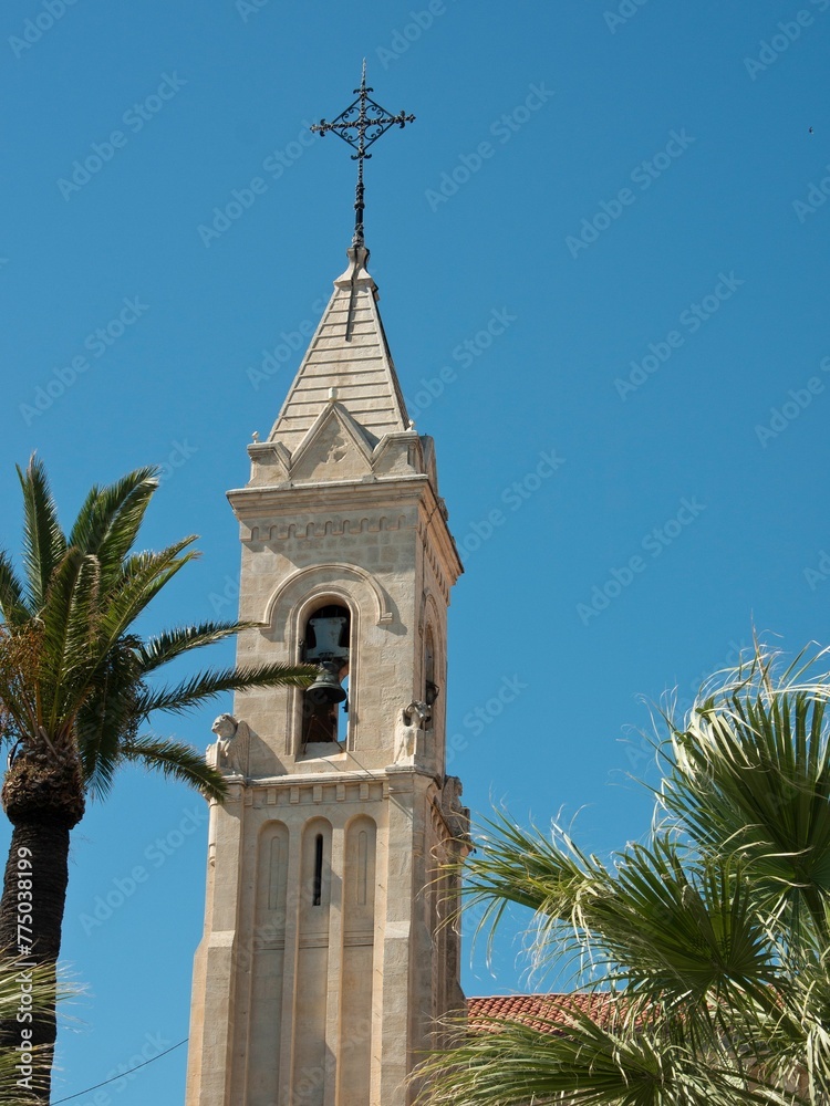 Vertical shot of the stone bell tower of a church in Sanary Sur Mer, France with trees and blue sky