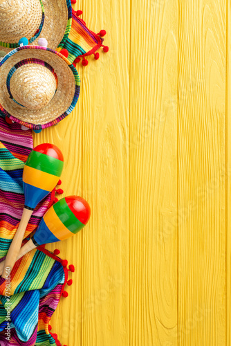 Colorful Cinco de Mayo vertical scene: top view of sombreros and maracas. Vibrant serape adorn the yellow wooden desk. Text-friendly space