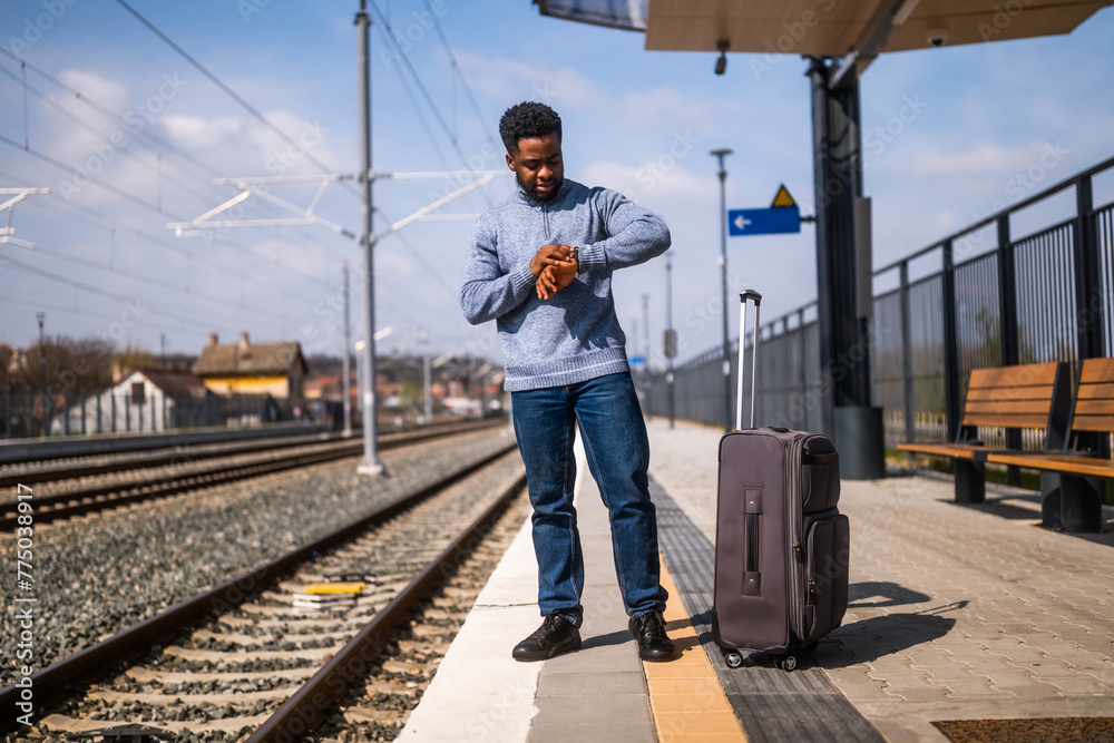 Worried man looking at his clock while standing with suitcase on a railway station. Worried man looking at his clock while standing with suitcase on a railway station.