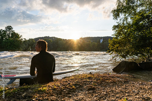 A young surfer by Aare River gazes at sunset, enjoying calm.
