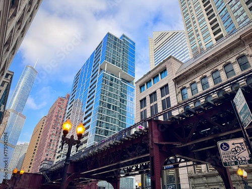 low angle view of the steel structure of the Chicago skytrain in a street in the Loop with a lit street lamp and the buildings of the center in the background
