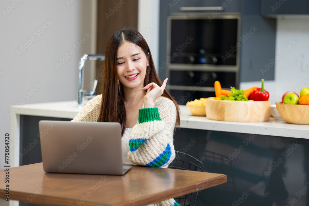 Happy woman using laptop - young Asian woman studying while sitting at table online learning by laptop computer at home Happy woman using laptop - young Asian woman studying while sitting at table online learning by laptop computer at home