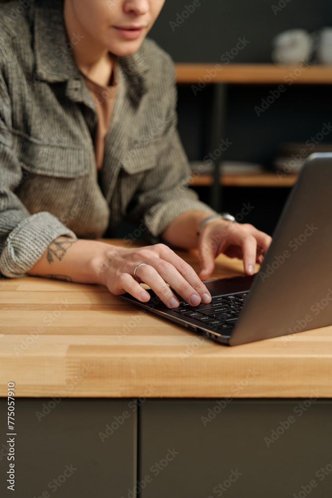 Naklejka premium Hands of young female designer or solopreneur typing on laptop keyboard by counter while organizing work in cafe after refit