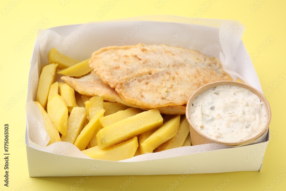 Delicious fish and chips with tasty sauce in paper box on yellow table, closeup Delicious fish and chips with tasty sauce in paper box on yellow table, closeup