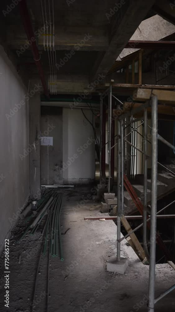 Interior of an unfinished construction site with exposed piping and scaffolding. Building under construction process overview, walking inside. Vertical orientation. Interior of an unfinished construction site with exposed piping and scaffolding. Building under construction process overview, walking inside. Vertical orientation.