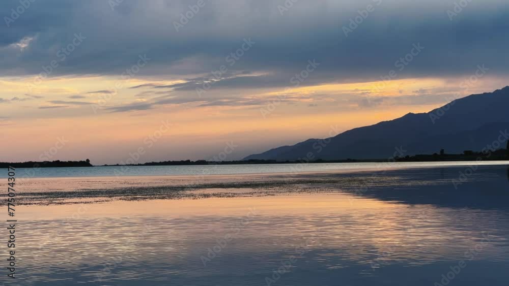 View of Issyk-Kul mountain lake at sunset, Kyrgyzstan. Waves splash on the beach with rocks. A calm, peaceful natural background. Sunset on the lake overlooking the Tien Shan Mountains. 4K