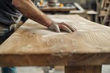 A close-up image capturing the precise moment an artisan's hand moves a sanding block across the rich, textured grain of a wooden surface. 