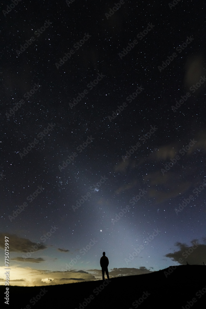 A stargazer looking into the night sky in the middle silhuette showing the zodiacal light in the sky.