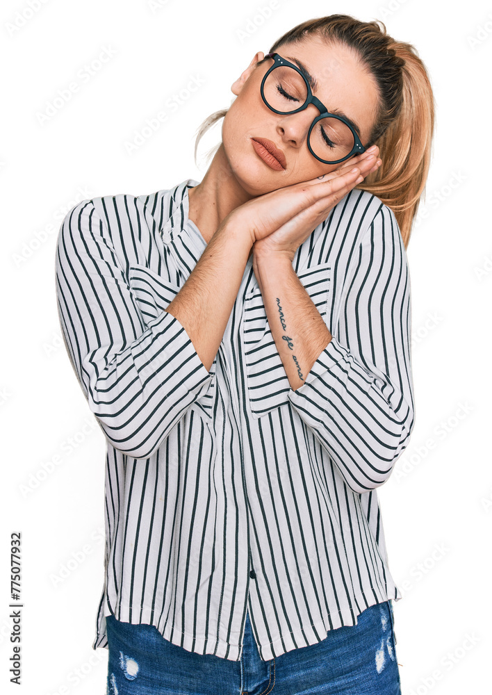 Young caucasian woman wearing business shirt and glasses sleeping tired dreaming and posing with hands together while smiling with closed eyes.