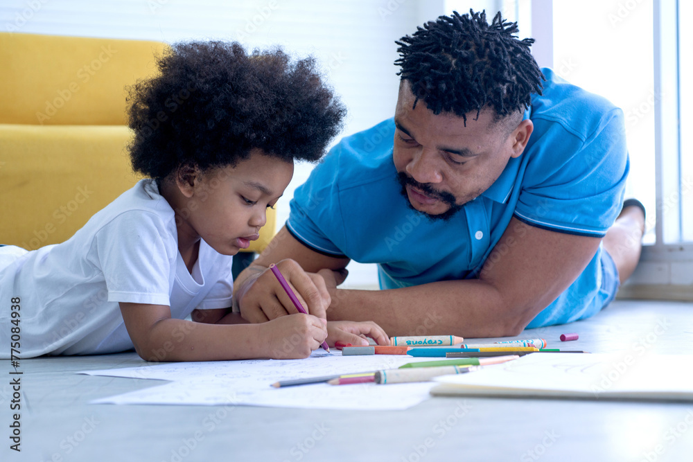 African father and son lying and drawn pictures on floor in living room, emotional positive father participates in home activities with his son, Father's day African father and son lying and drawn pictures on floor in living room, emotional positive father participates in home activities with his son, Father's day