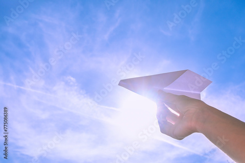 hand holding white paper plane against bright sky