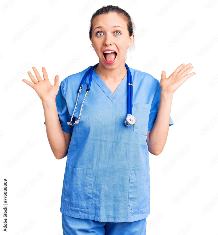 Young beautiful blonde woman wearing doctor uniform and stethoscope celebrating crazy and amazed for success with arms raised and open eyes screaming excited. winner concept