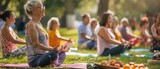 Several healthy, mature people are doing yoga in an outdoor park, on green grass, with yoga mats. Men and women in yoga class are smiling and happy as they exercise on the grass.