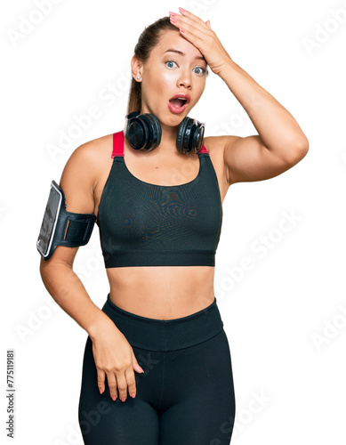 Beautiful blonde woman wearing gym clothes and using headphones surprised with hand on head for mistake, remember error. forgot, bad memory concept.