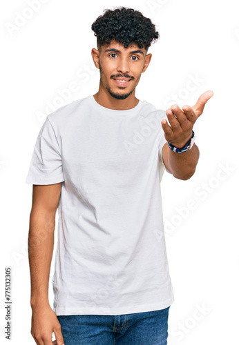 Young arab man wearing casual white t shirt smiling friendly offering handshake as greeting and welcoming. successful business.