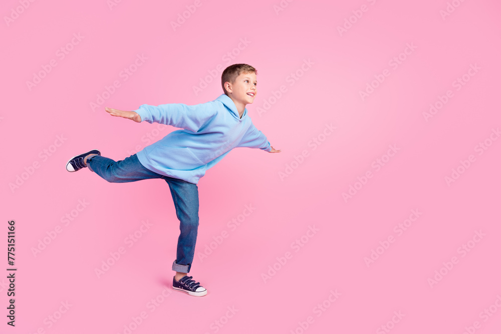 Full size profile portrait of cheerful schoolchild stand one leg hands wings look empty space isolated on pink color background
