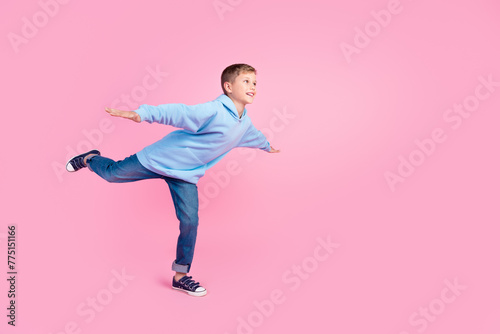 Full size profile portrait of cheerful schoolchild stand one leg hands wings look empty space isolated on pink color background