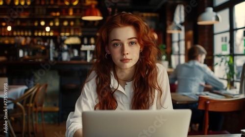 Young girl working on laptop, girl freelancer or student with laptop in cafe at table looking in camera