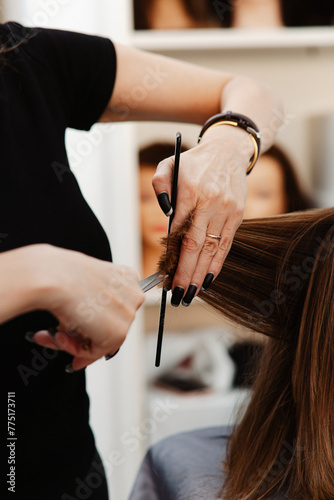 A professional hairstylist in the process of giving a precise haircut, holding scissors and a section of hair.
