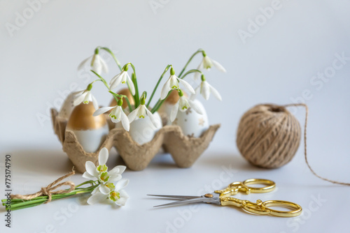 Minimal Easter concept. Festive spring mood, paper box with Easter eggs in light colors and snowdrop flowers.