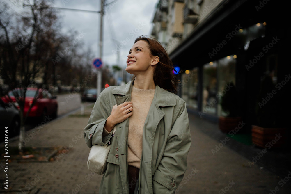Fototapeta premium beautiful cheerful woman walks around the city in a gray coat in the spring near the shops