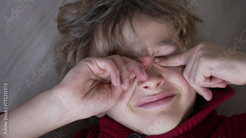 Tired young boy rubbing eyes with hands, close-up face of tired kid touching face with itchy eye photo