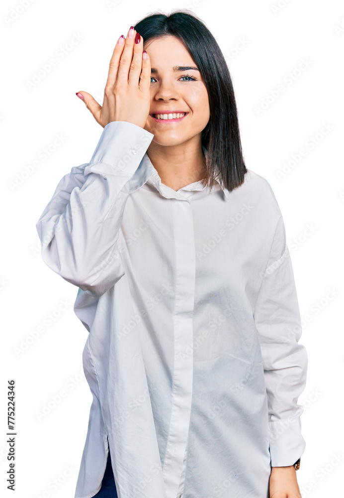 Young brunette woman with blue eyes wearing oversize white shirt covering one eye with hand, confident smile on face and surprise emotion. Young brunette woman with blue eyes wearing oversize white shirt covering one eye with hand, confident smile on face and surprise emotion.