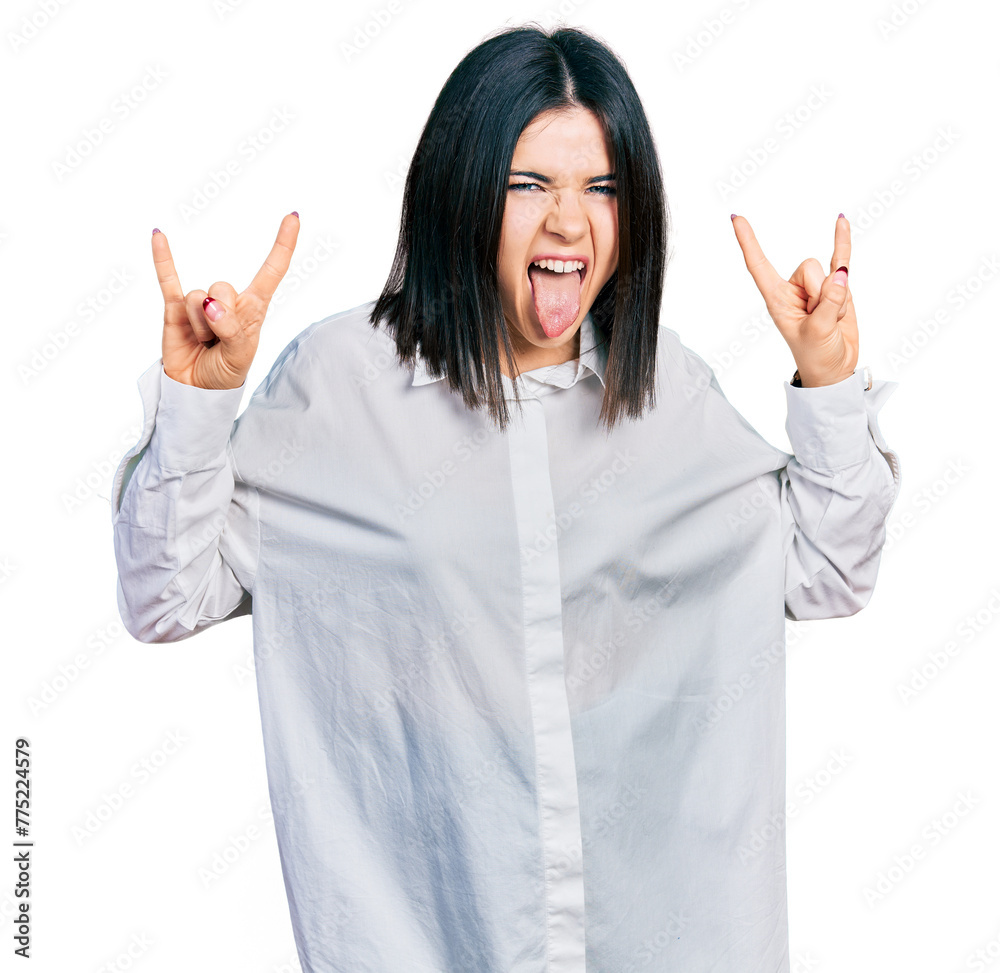 Young brunette woman with blue eyes wearing oversize white shirt shouting with crazy expression doing rock symbol with hands up. music star. heavy music concept. Young brunette woman with blue eyes wearing oversize white shirt shouting with crazy expression doing rock symbol with hands up. music star. heavy music concept.