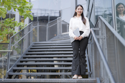 Professional woman in a white shirt poses confidently by the stairs © Naypong Studio