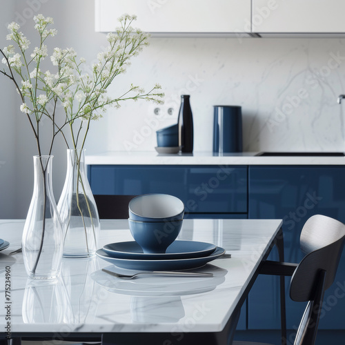 Empty and clean marble dining table in scandinavian kitchen. Modern monochrome interior with blue drawers on wooden furniture. Tablewear and vases with flowers. photo