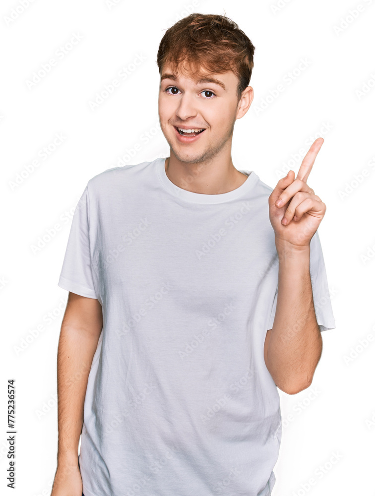 Young caucasian man wearing casual white t shirt showing and pointing up with finger number one while smiling confident and happy. Young caucasian man wearing casual white t shirt showing and pointing up with finger number one while smiling confident and happy.