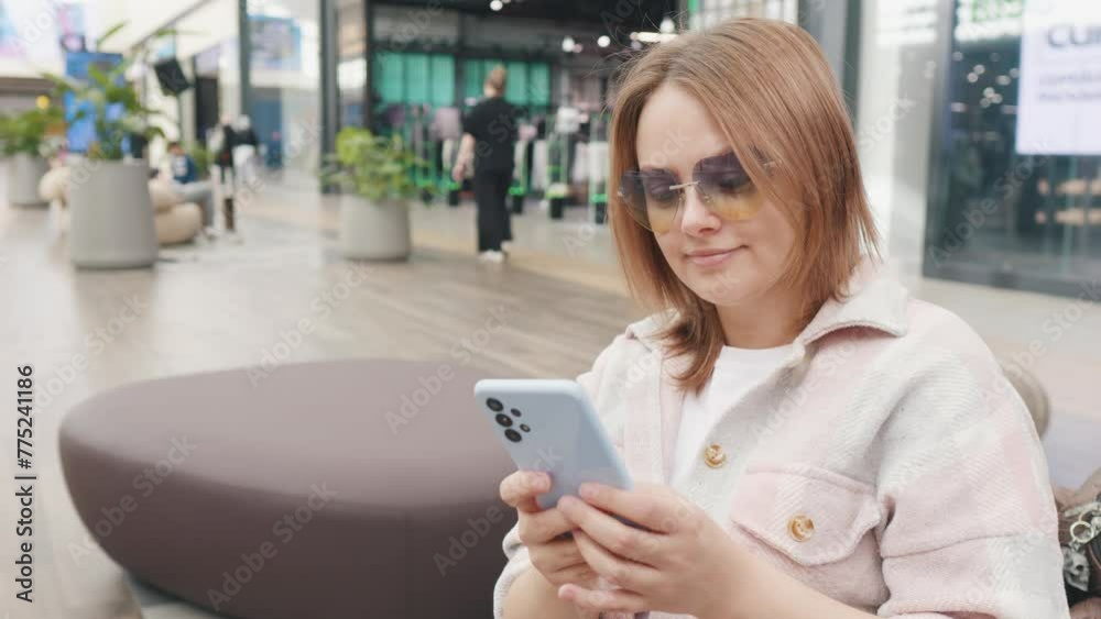 Girl shopaholic text messaging in the hall of shopping mall. Girl shopaholic text messaging in the hall of shopping mall.