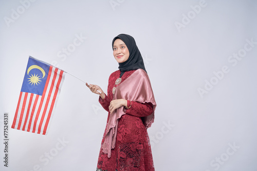 Beautiful Asian girl wearing traditional kebaya with hijab, happily holding Malaysian flag isolated over white background. Independence day, new year nationalism concept.